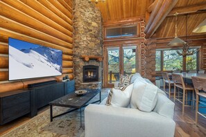 A log cabin interior with a stone fireplace, a television mounted on the wall, and a sofa with pillows. - Newly Furnished 3BR Ski Townhome Sleeps 8 + Private Hot Tub (Mountain Village)