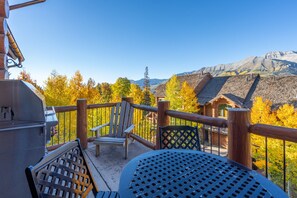 A wooden deck with a grill, a chair, and a table overlooking a mountainous landscape with autumn foliage. - Newly Furnished 3BR Ski Townhome Sleeps 8 + Private Hot Tub (Mountain Village)