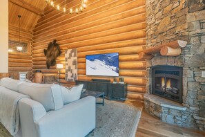 A log cabin interior with a stone fireplace, a mounted fur, a television, and a cozy seating area. - Newly Furnished 3BR Ski Townhome Sleeps 8 + Private Hot Tub (Mountain Village)