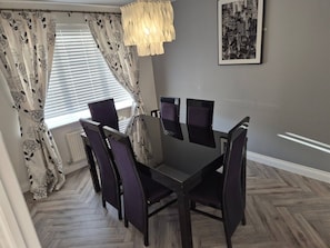 A dining area with a table and chairs, a window with blinds, and a hanging light fixture. - Wrexham Retreat Villa, 4 bedrooms, 4 beds, 3 Baths (Brymbo)
