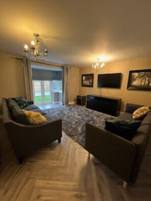 A living room with a sofa set, a flat-screen TV, and a chandelier. - Wrexham Retreat Villa, 4 bedrooms, 4 beds, 3 Baths (Brymbo)
