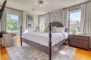 Un dormitorio con una cama con dosel, una mesita de noche con lámpara, un aparador y una silla.
