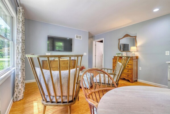 Una habitación con cama, una silla de madera, un aparador, un televisor y una ventana con cortinas.
