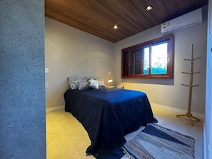Ein Schlafzimmer mit einem Bett, einem Nachttisch, einer Lampe, einem Fenster mit Rollläden und einer Holzleiter.