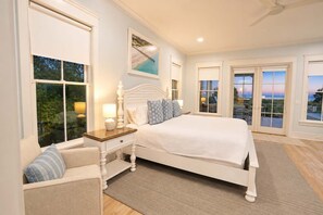 A bedroom with a large bed, a nightstand, a chair, and a view of the outdoors through the windows. - 3908 Palm Boulevard, Isle of Palms (Isle of Palms)