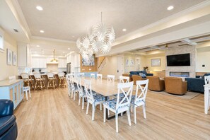 A spacious living area with a wooden dining table, white chairs, a blue sofa, and a flat-screen TV mounted on the wall. - 3908 Palm Boulevard, Isle of Palms (Isle of Palms)