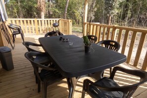 Una terraza de madera con una mesa, sillas, un bote de basura y una planta en maceta.