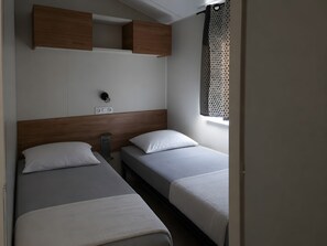 Habitación de hotel con dos camas, cabecero de madera, mesita de noche pequeña, toma de corriente y ventana con cortina de lunares.