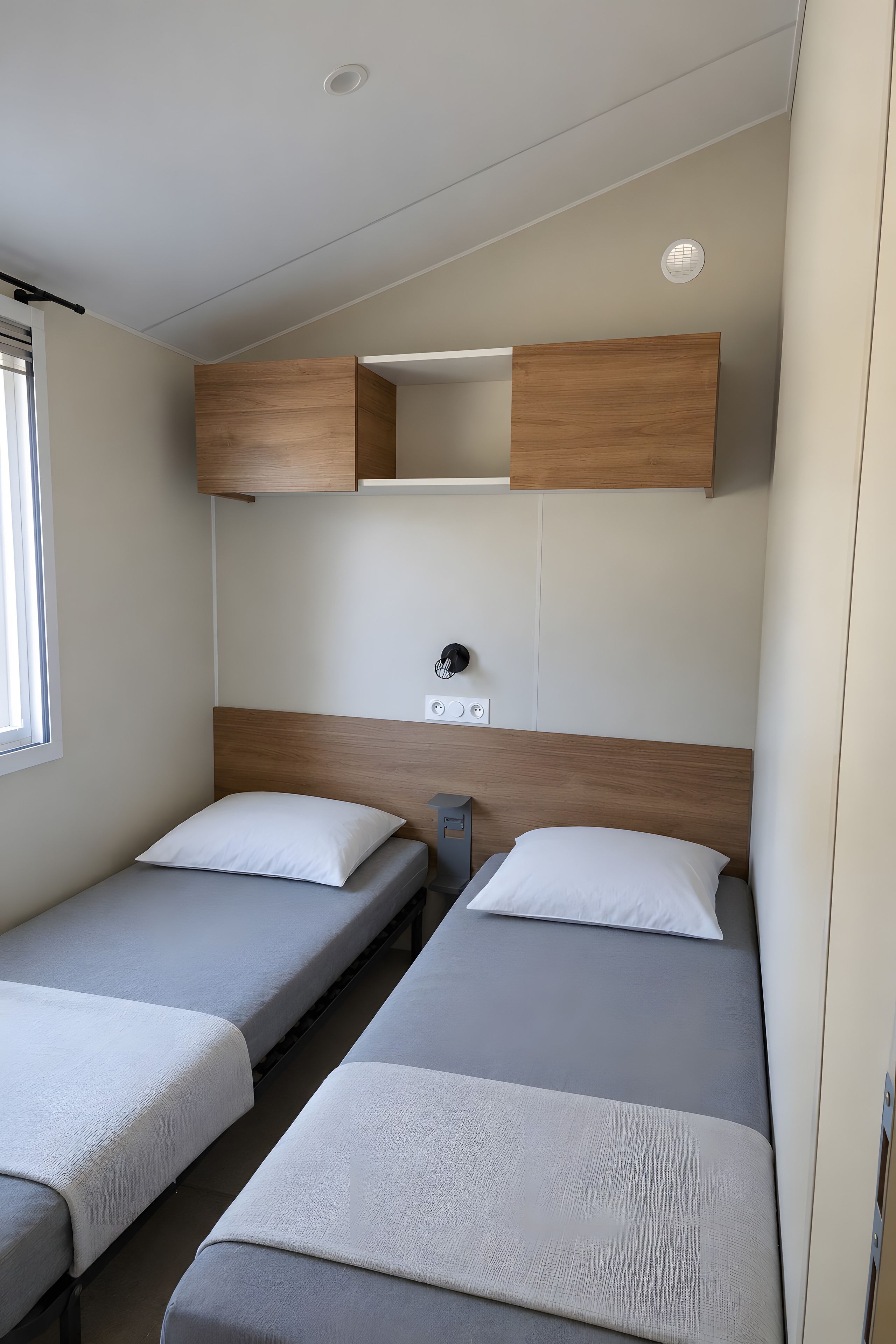Ein kleines Zimmer mit zwei Einzelbetten, einem kleinen Tisch und einem an der Wand befestigten Regal.