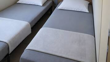 Ein kleines Zimmer mit zwei Einzelbetten, einem kleinen Tisch und einem an der Wand befestigten Regal.