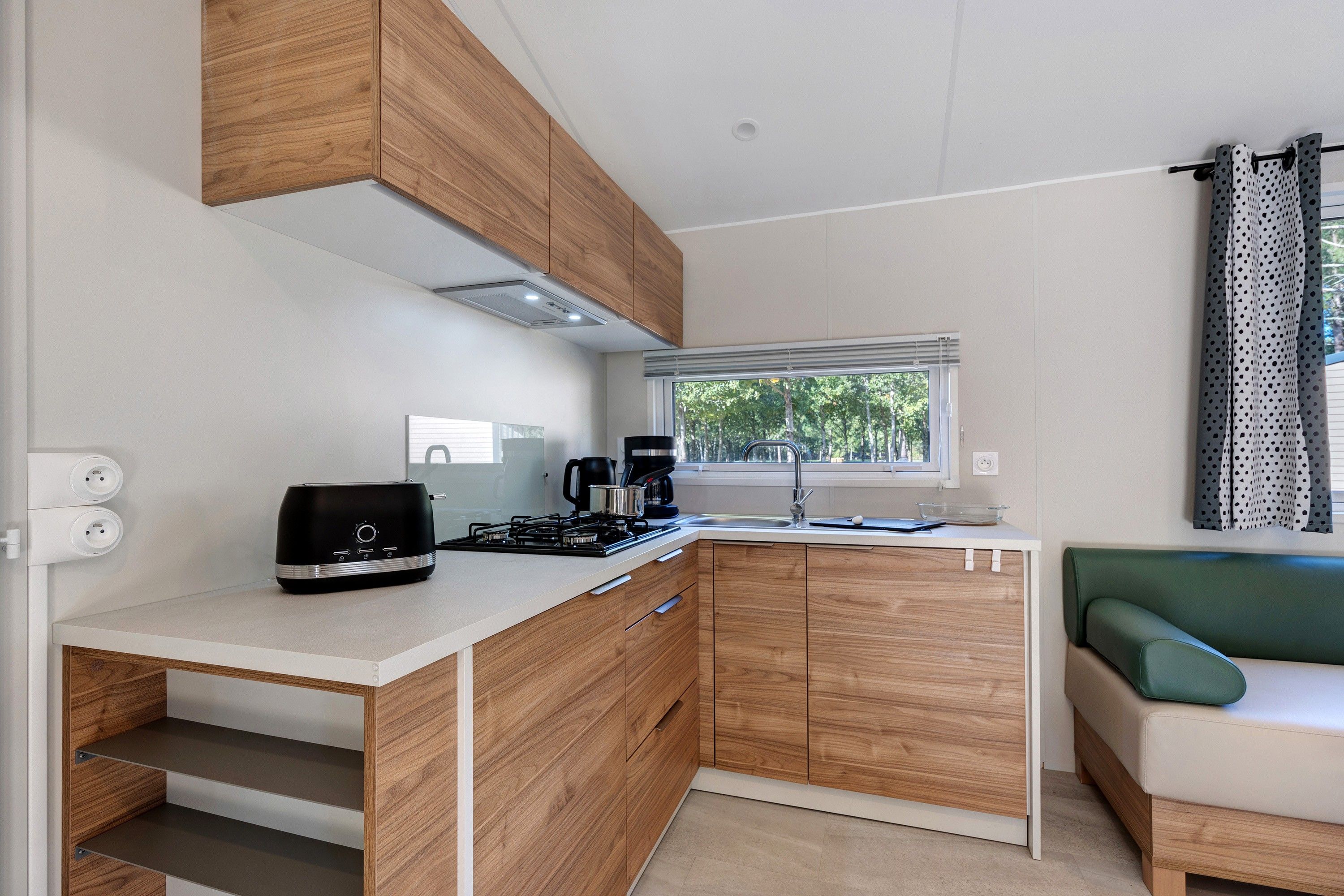 Una kitchenette compacta con estufa a gas, cafetera y ventana con vista a árboles.