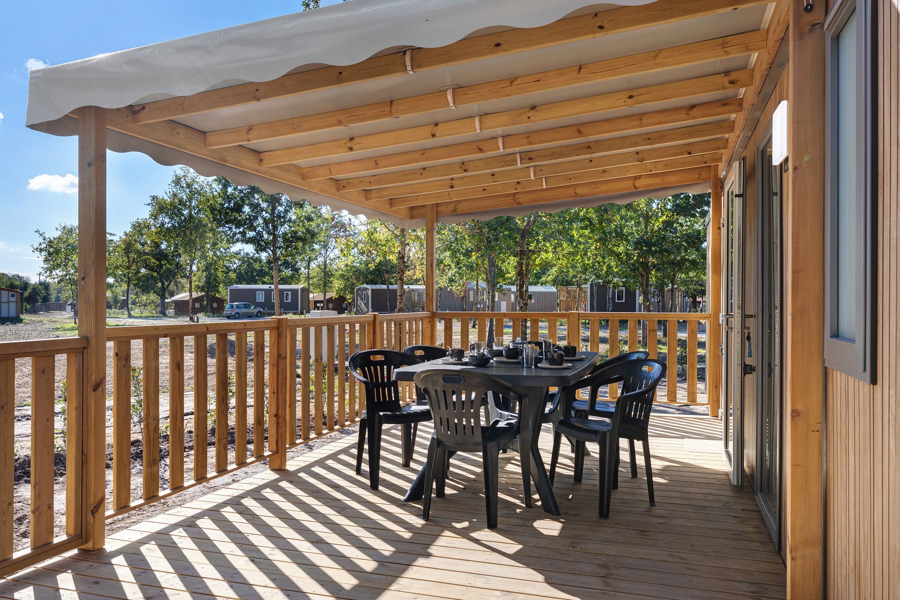 Een overdekt terras buiten met een tafel en stoelen, omgeven door een houten balustrade.