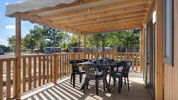 Een overdekt terras buiten met een tafel en stoelen, omgeven door een houten balustrade.