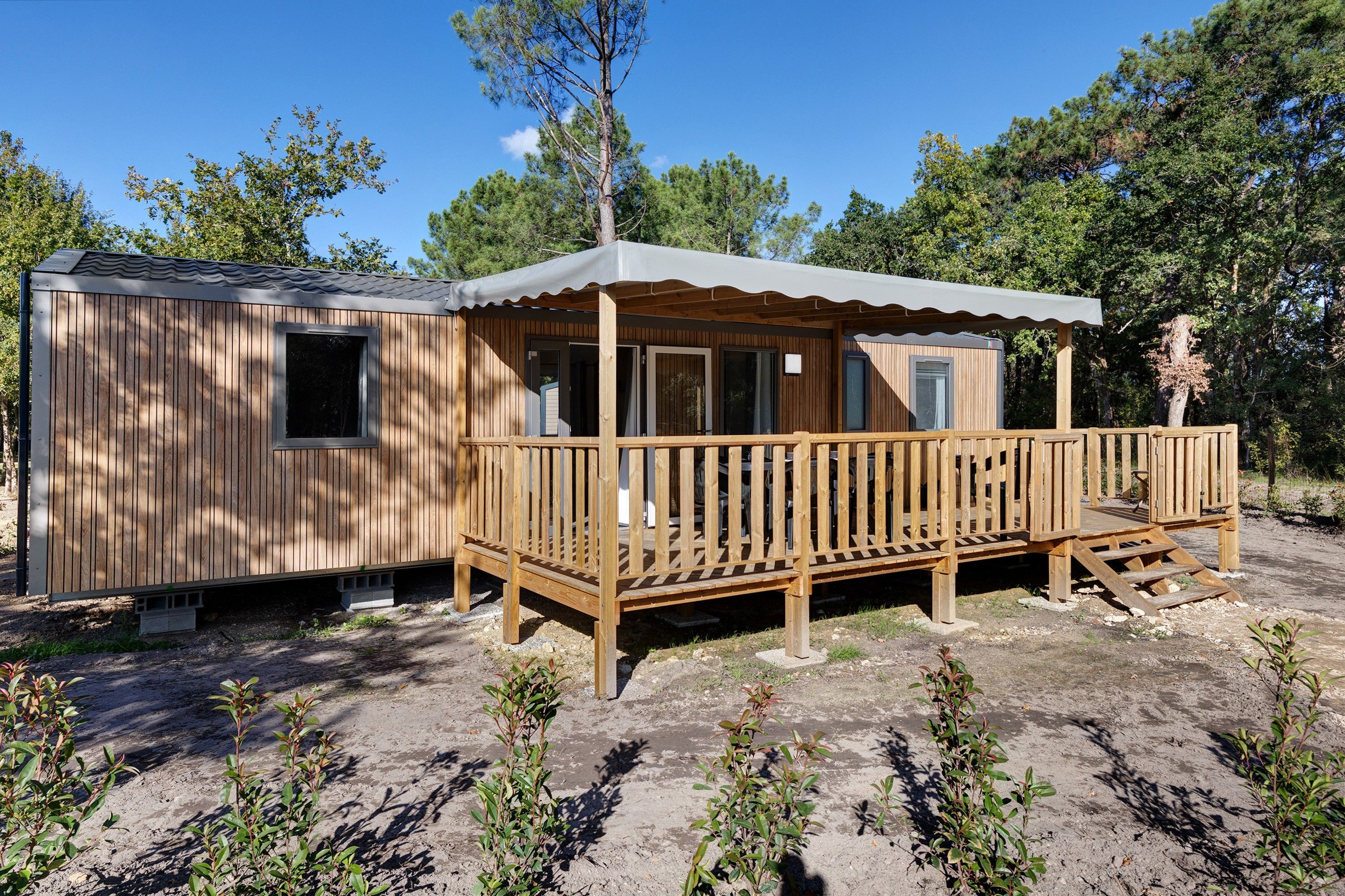 Een houten blokhut met een veranda en een overdekt terras, omgeven door bomen.