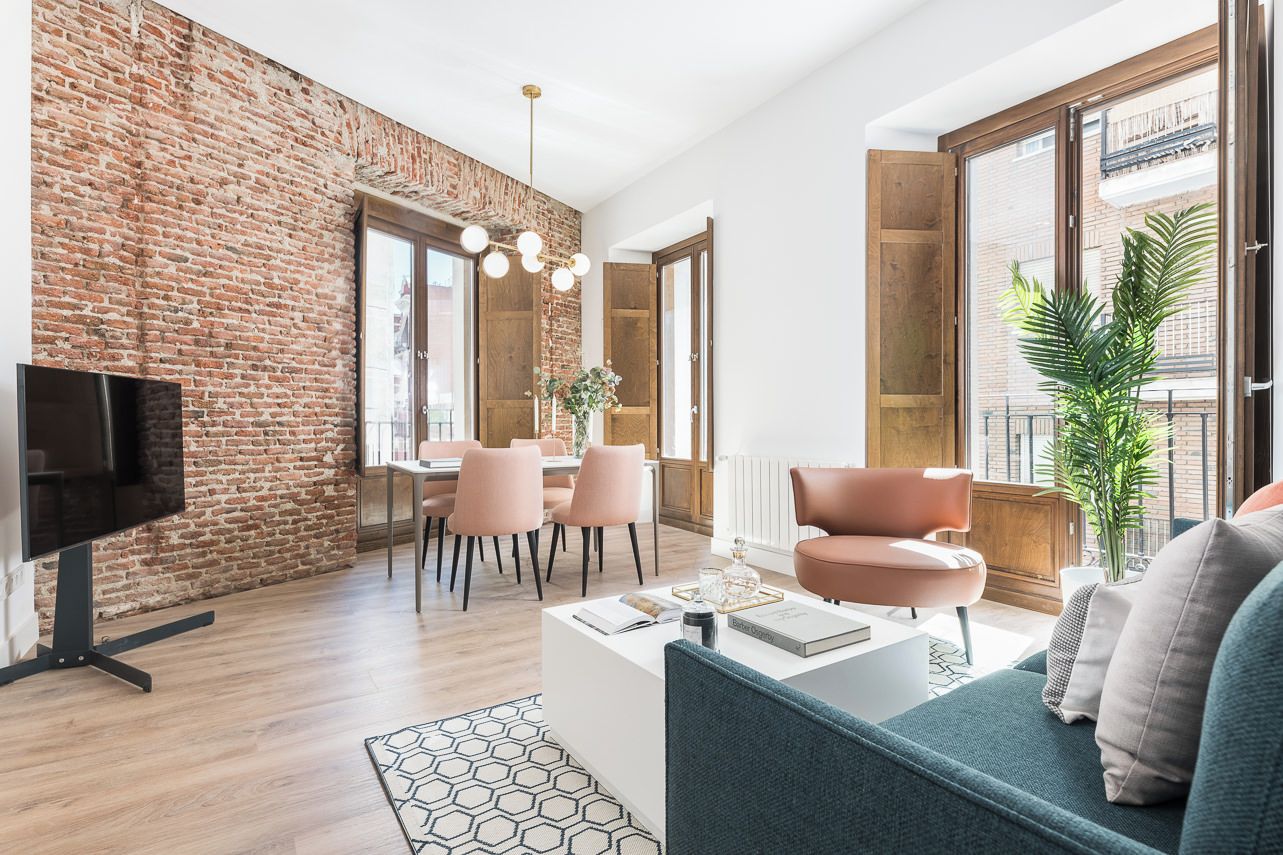 A modern living room with a brick wall, a dining area with pink chairs, and a large window with a view.