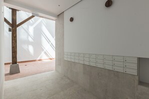 A room with a concrete floor, a wooden beam structure, a white wall with a row of mailboxes, and a door leading to another space. - Santa Ana XXXIV / XLII (TUR) (Madrid)