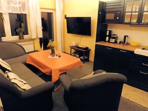 A small living area with a sofa, a table, and a kitchen area with cabinets and a microwave. - Apartment 'Petronela' with Lake View, Private Terrace and Wi-Fi (Waren (Müritz))