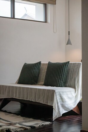 Cama com colcha listrada e duas almofadas verdes, luminária pendente e janela sobre a cama.