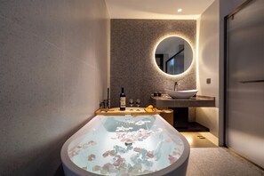 Un bany modern amb una banyera autònoma, un mirall rodó i un lavabo.