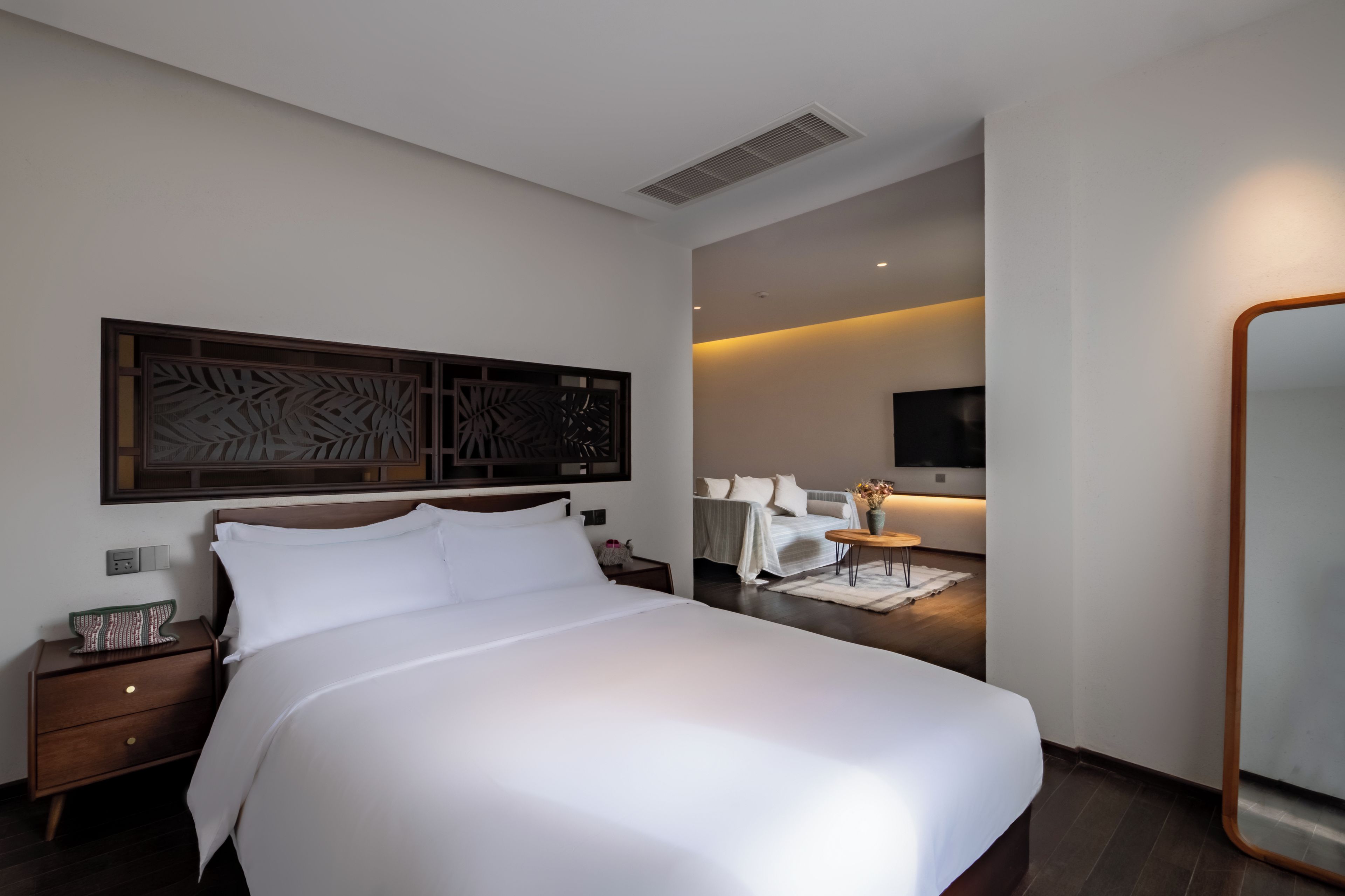 A hotel room with a large bed, a nightstand, a wall-mounted TV, and a mirror.