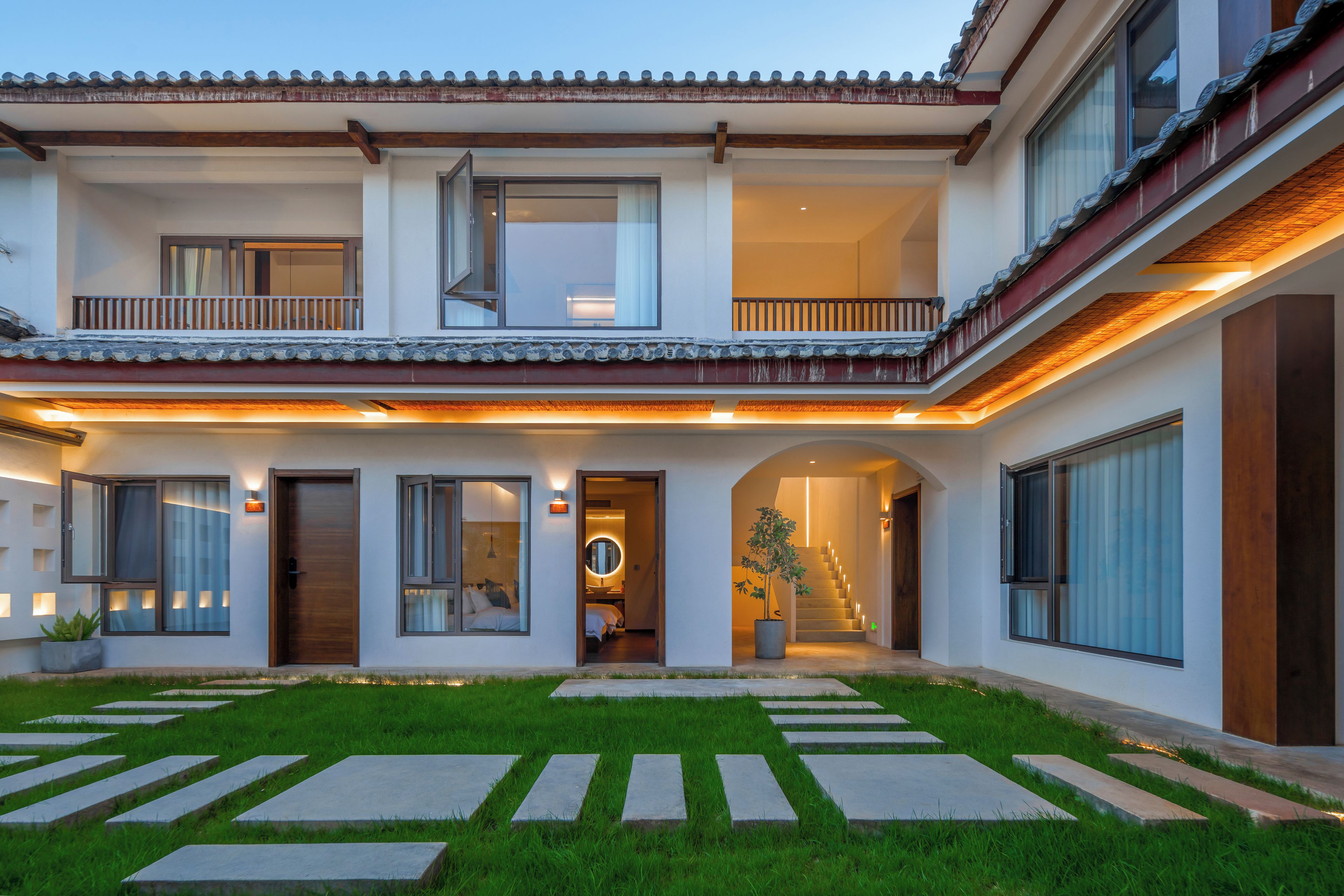 Uma casa de dois andares com varanda, escada e entrada bem iluminada.