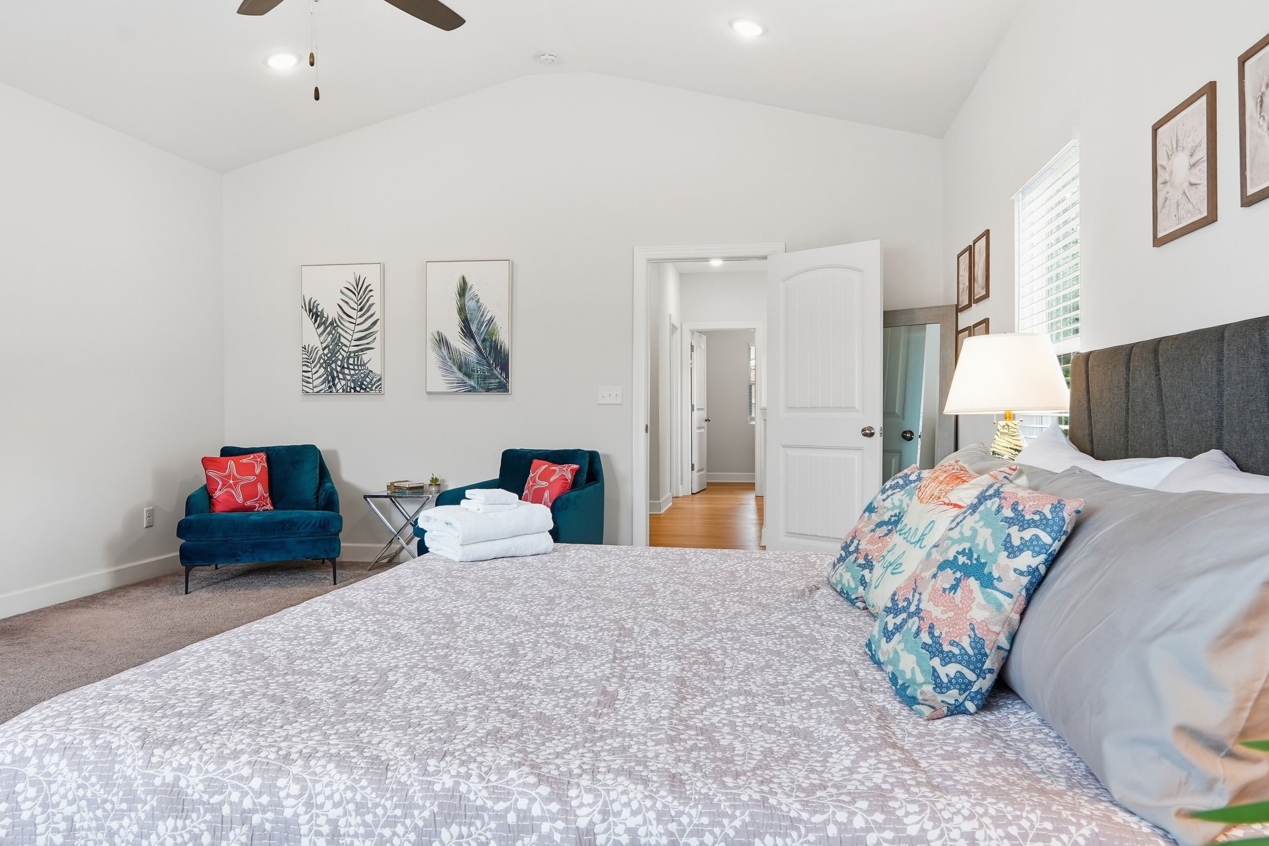 A spacious bedroom with a large bed, two armchairs, a side table, and artwork on the walls.