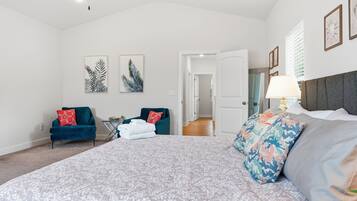 A spacious bedroom with a large bed, two armchairs, a side table, and artwork on the walls.