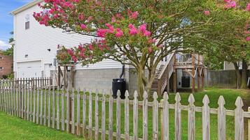 A white house with a wooden deck and a pink flowering tree.