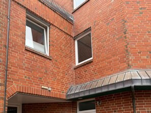 A multi-story brick building with two visible windows, a metal awning, and a door. - Fiete Deppe House - Apt. 1 (Wyk auf Foehr)
