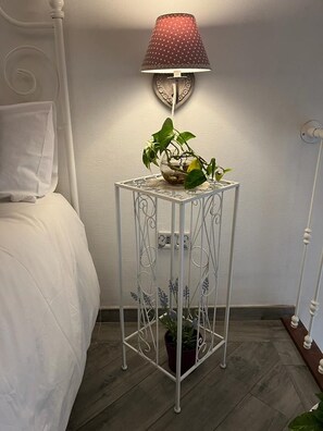 Ein nachtisches aus weißem Metall mit rotem Lampenschirm, einem Topfpflanzen und einem weißen Bett mit weißem Kopfkissen.