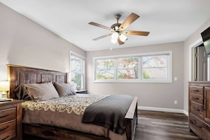A bedroom with a bed, nightstands, a dresser, a ceiling fan, and windows. - 4BR Grass Lake Cottage (Grass Lake)