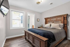 A bedroom with a wooden bed, a nightstand, a window, and a door. - 4BR Grass Lake Cottage (Grass Lake)