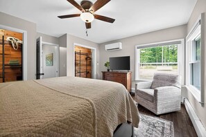 Un dormitorio con cama, una silla, ventilador de techo, televisión y ventana.