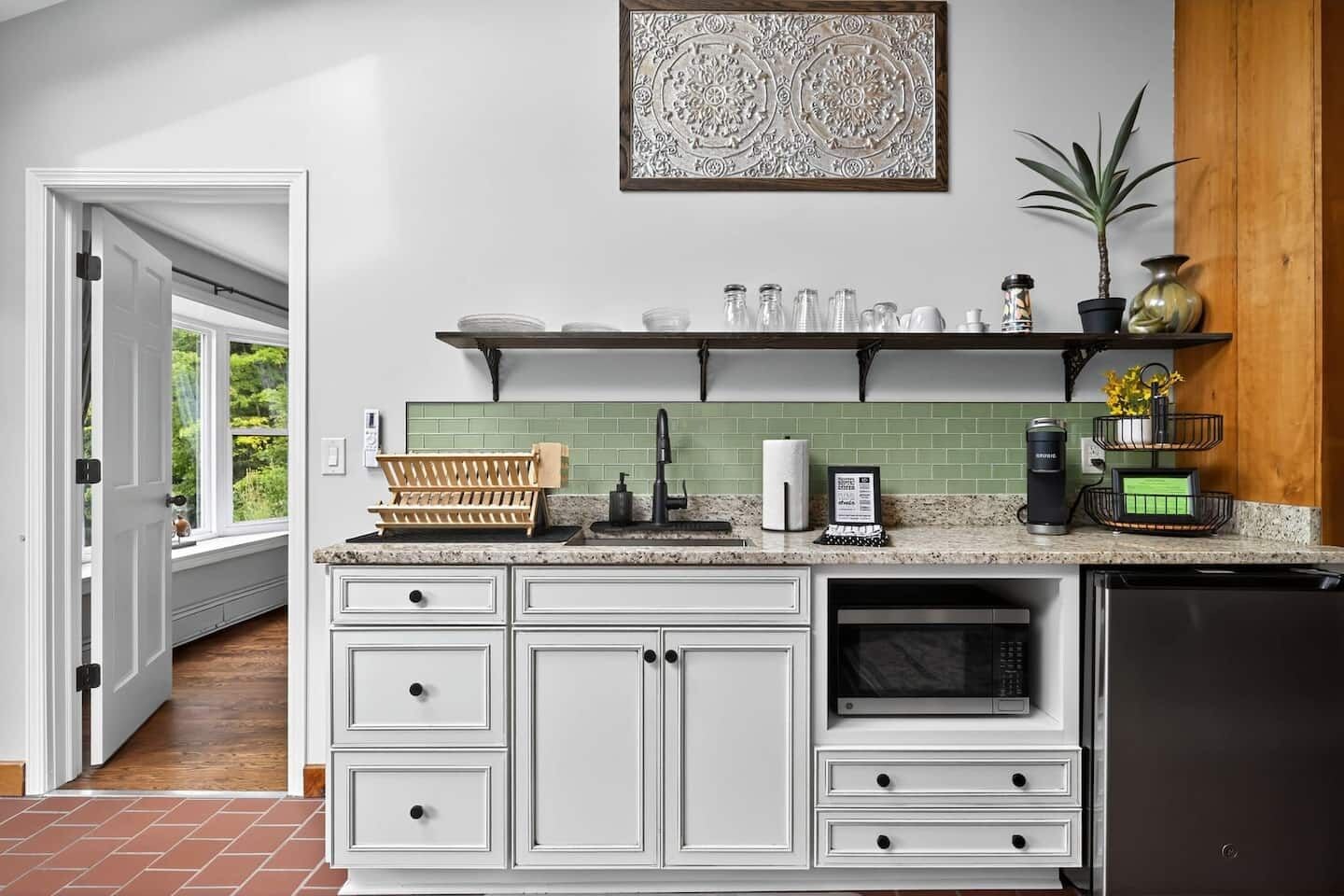 A kitchen with white cabinetry, a green backsplash, and a coffee machine on the counter.