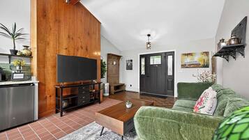 A living room with a television, a green sofa, a wooden cabinet, and a kitchen area with a dishwasher.