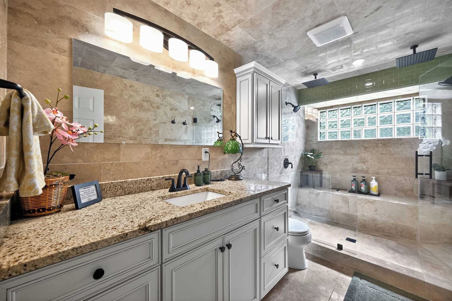 A modern bathroom with a granite countertop, a large mirror, and a shower area.