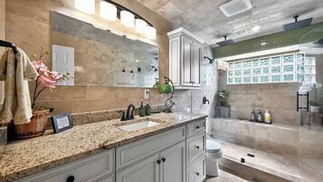 A modern bathroom with a granite countertop, a large mirror, and a shower area.