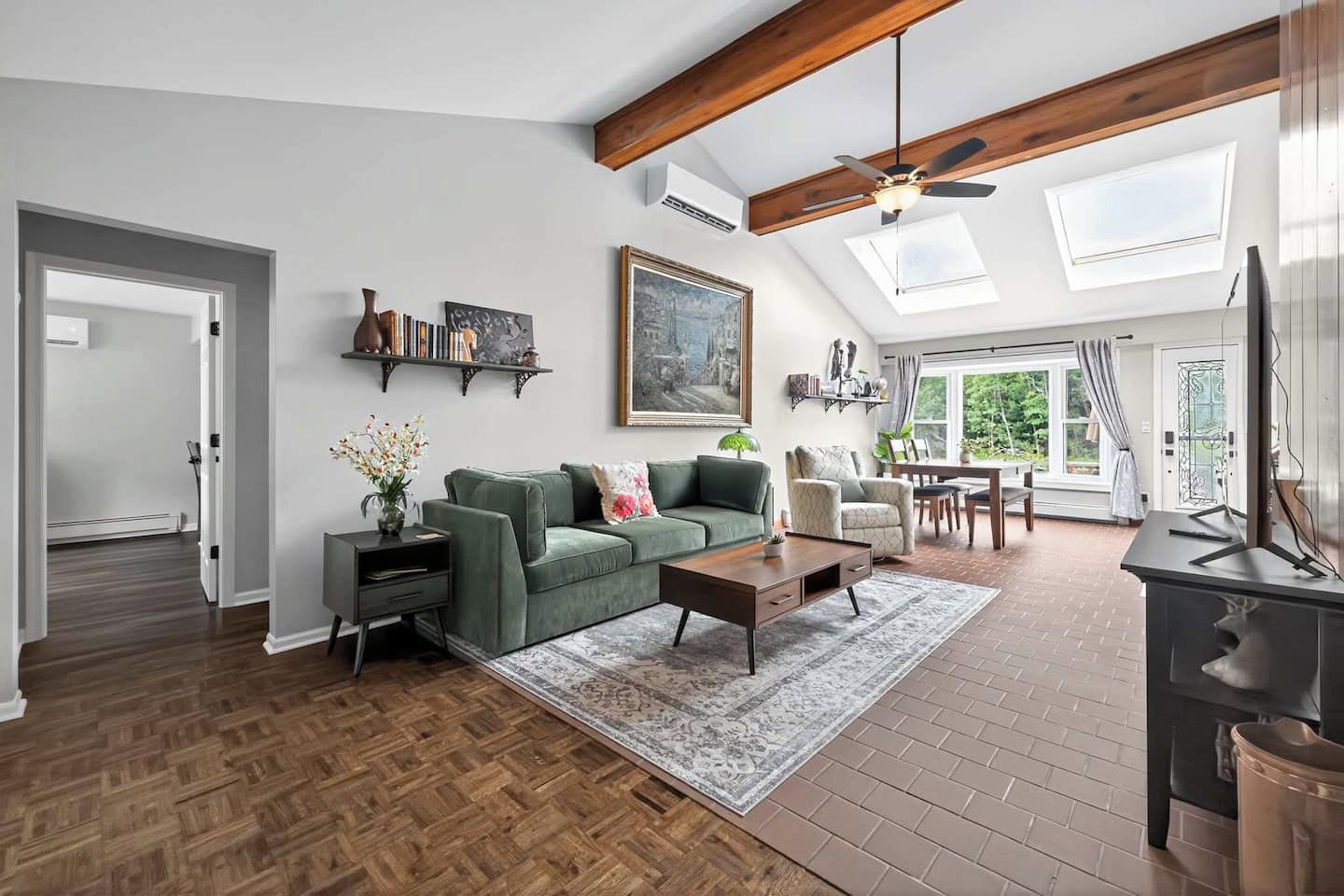A spacious living room with a herringbone floor, a green sofa, a coffee table, and a painting above the sofa.