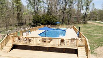A wooden deck with a swimming pool, surrounded by a fence and trees.