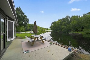 A patio with a table and chairs, overlooking a calm lake and surrounded by trees.
