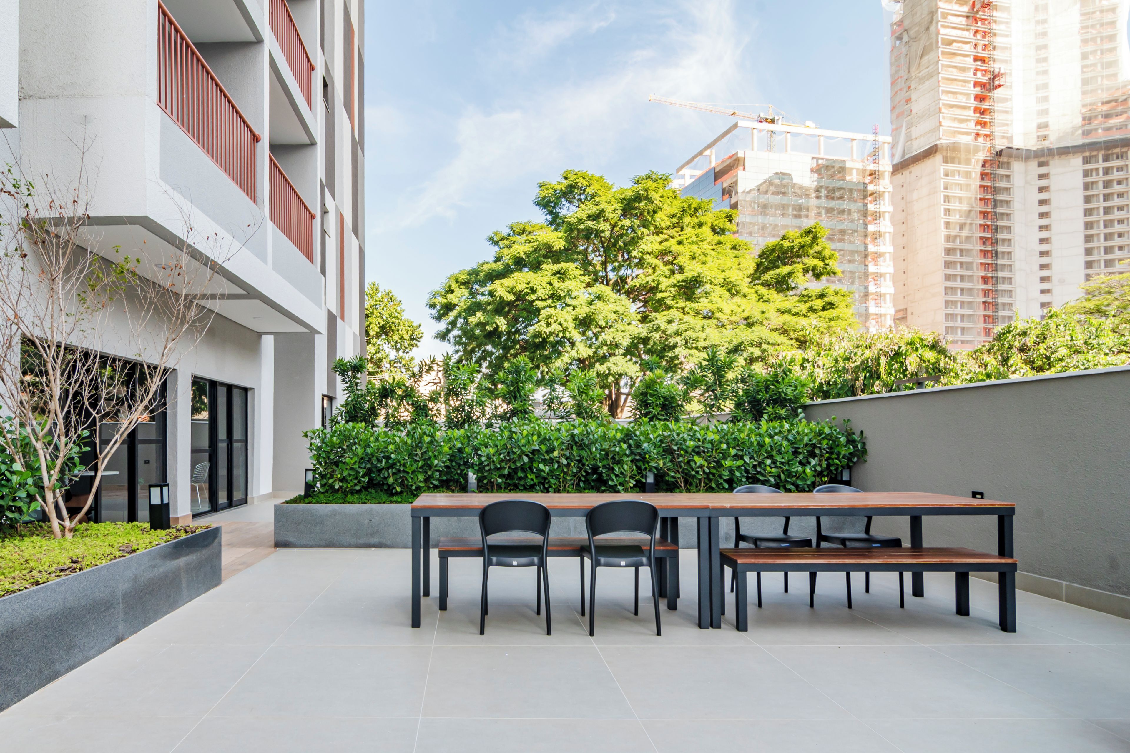 A modern outdoor seating area with a table and chairs, surrounded by greenery and a view of a construction site.