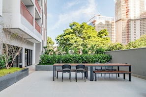 A modern outdoor seating area with a table and chairs, surrounded by greenery and a view of a construction site. - Becker by Bhomy (São Paulo)
