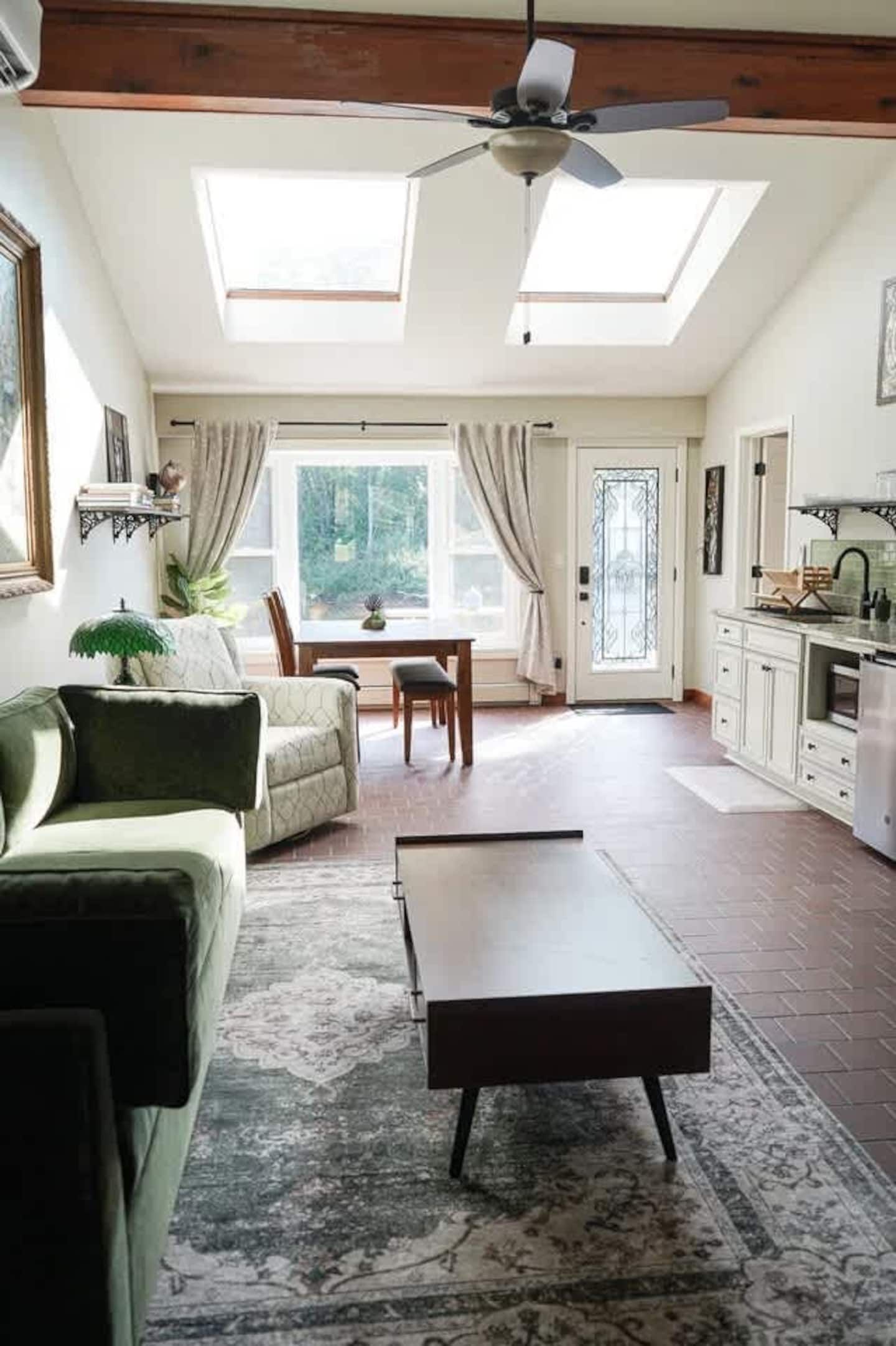 Un ampio soggiorno con ventola a soffitto, una zona pranzo con tavolo e sedie, e un angolo cottura con pensili e piano di lavoro.