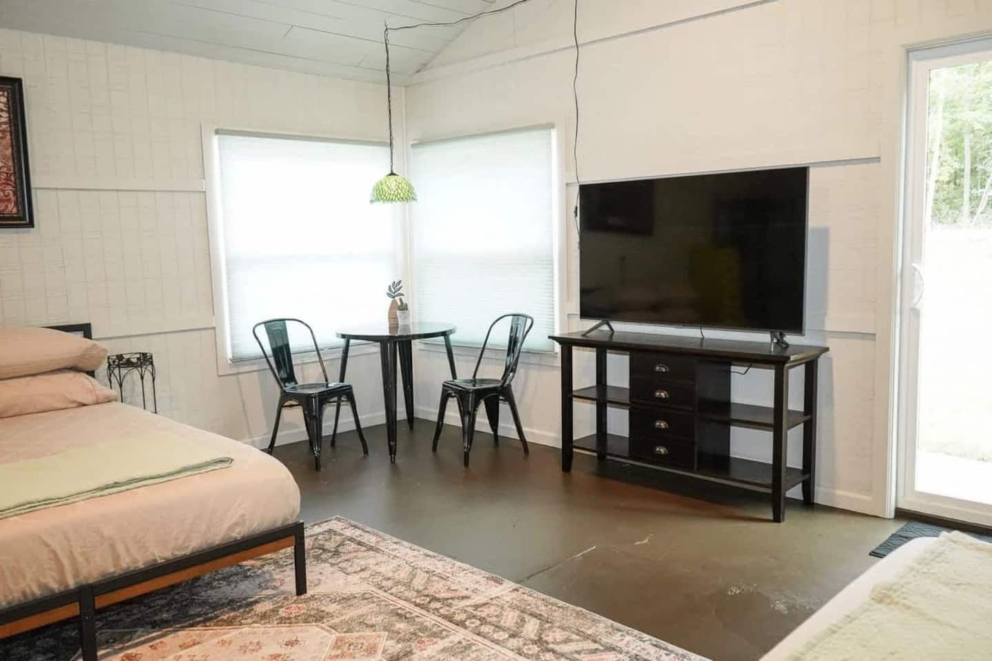 A bedroom with a bed, a desk with a TV, two chairs, and a window.