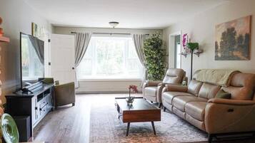 Ett vardagsrum med en soffa, ett soffbord, en tv och ett stort fönster med gardiner.