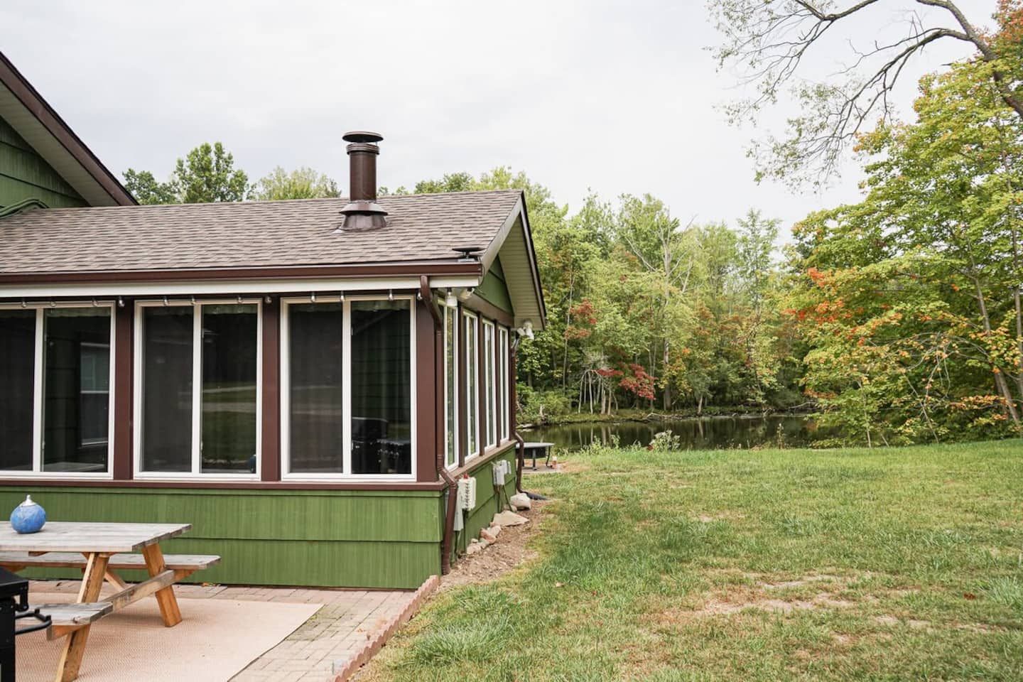 A house with a covered porch, a chimney, and a grassy yard with trees.
