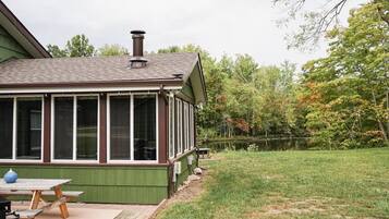 A house with a covered porch, a chimney, and a grassy yard with trees.