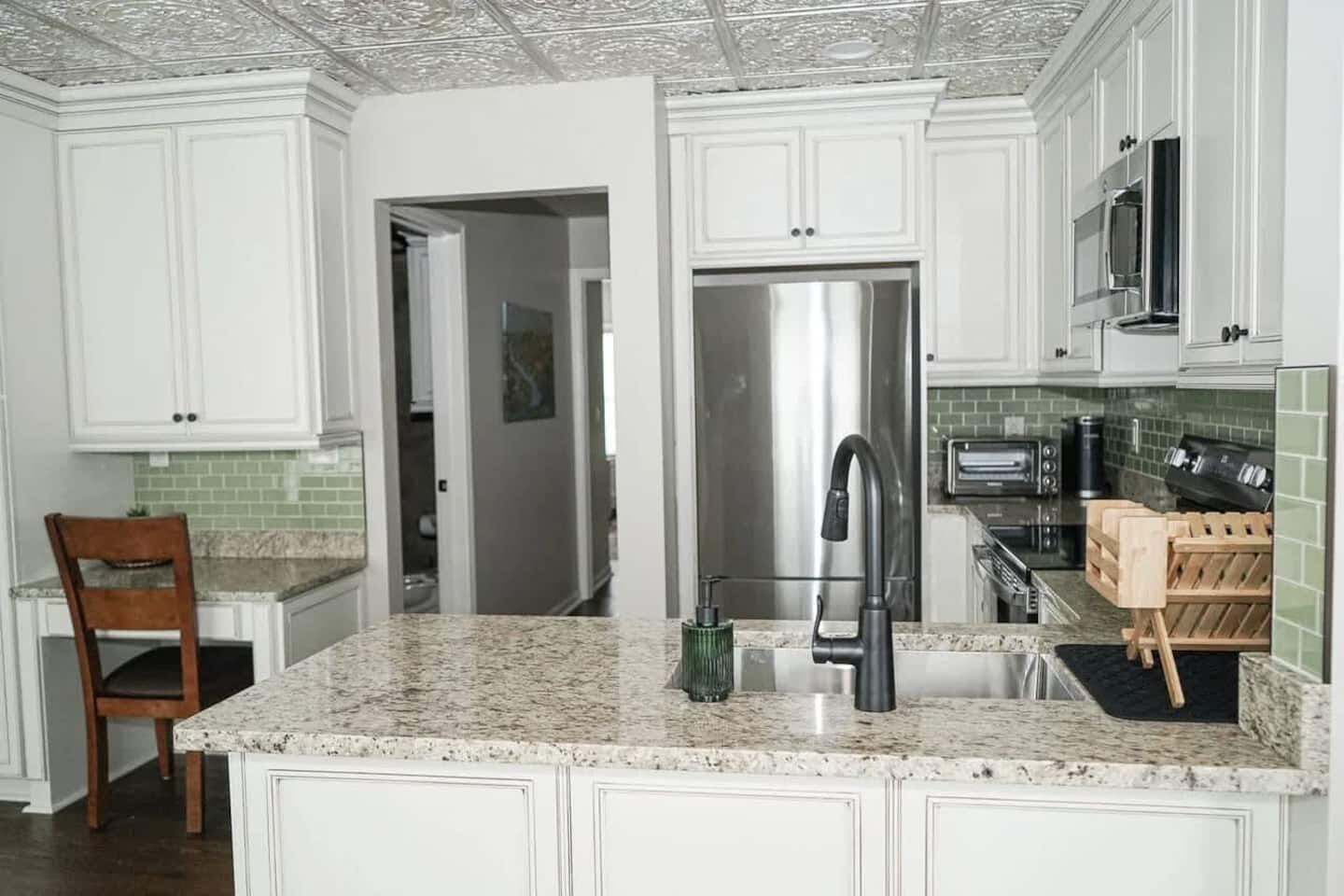 A kitchen with white cabinetry, a stainless steel refrigerator, a built-in oven, and a microwave.