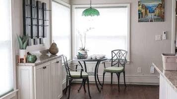 Una cocina con armarios blancos, una mesa de comedor con sillas, una lámpara colgante verde y un ventanal con vistas.