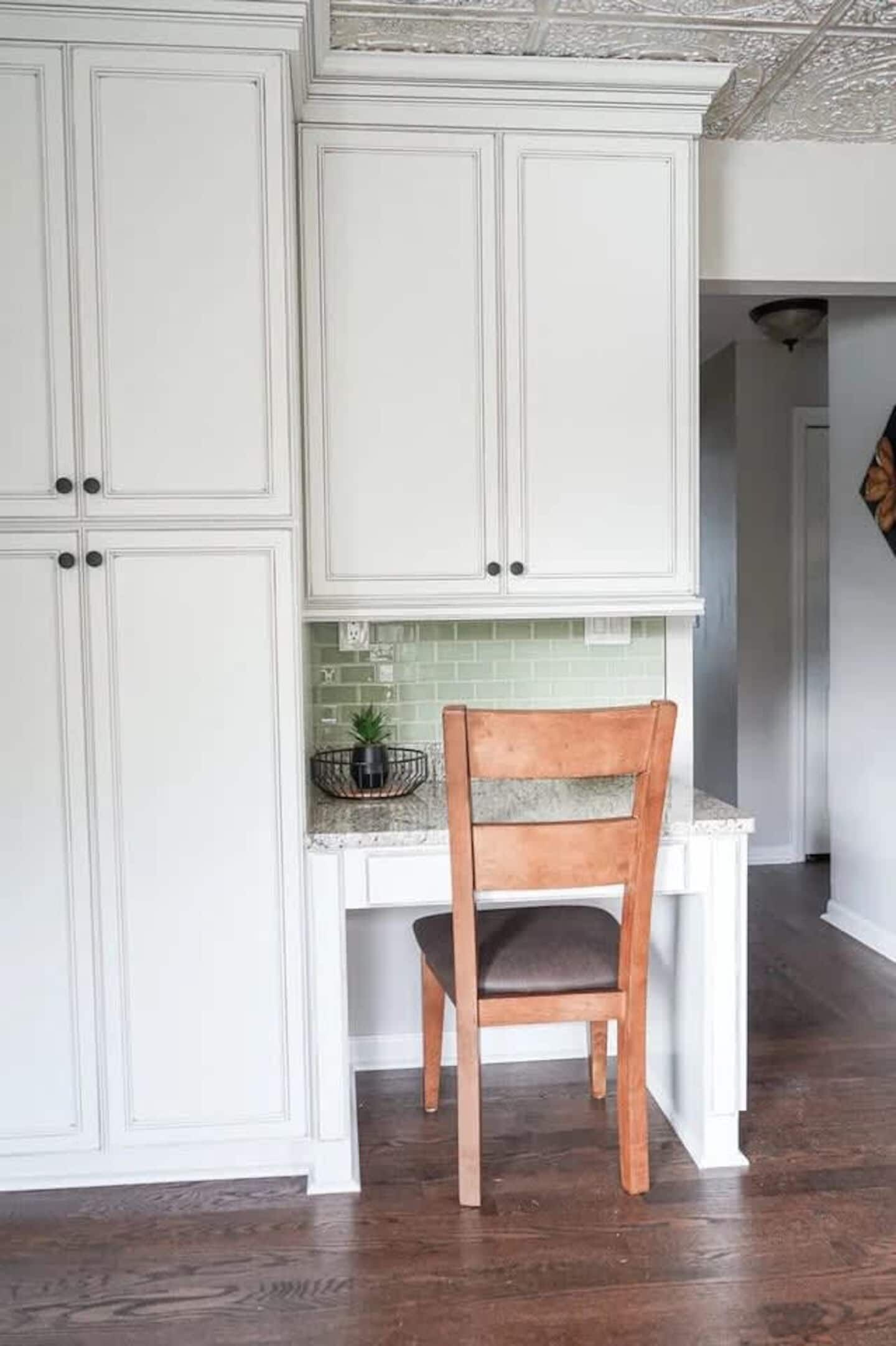 A kitchen with white cabinetry, a wooden chair, and a green backsplash.